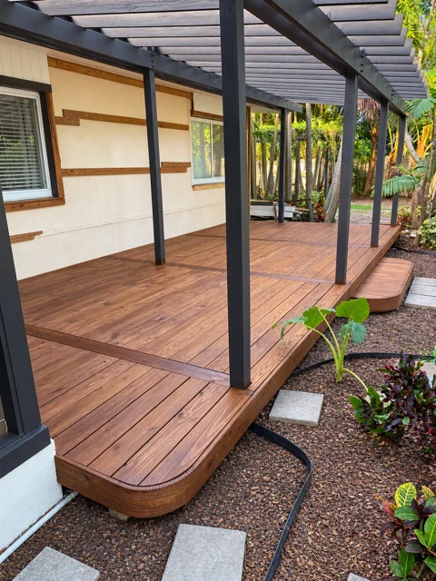 Custom stained wood deck with rounded corners beneath a dark pergola