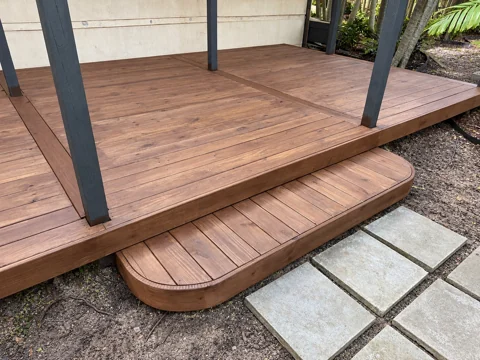 Rounded wood entry step and framed deck boards beside a stone path